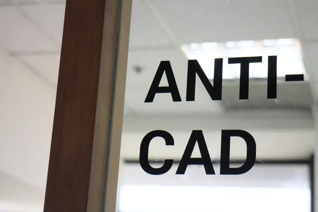 Text reading “ANTI-CAD” is displayed on a glass door or partition. The photo, taken from an angle, reveals part of the door frame and a blurred office interior featuring a modern kinetic ceiling in the background.