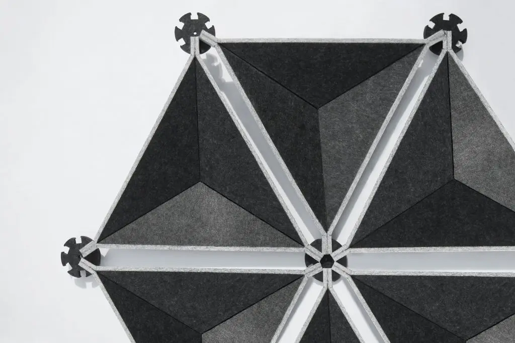 Geometric pattern made of dark gray and black felt triangles arranged in a hexagonal shape, connected at the corners with round, gear-like connectors on a white background.
